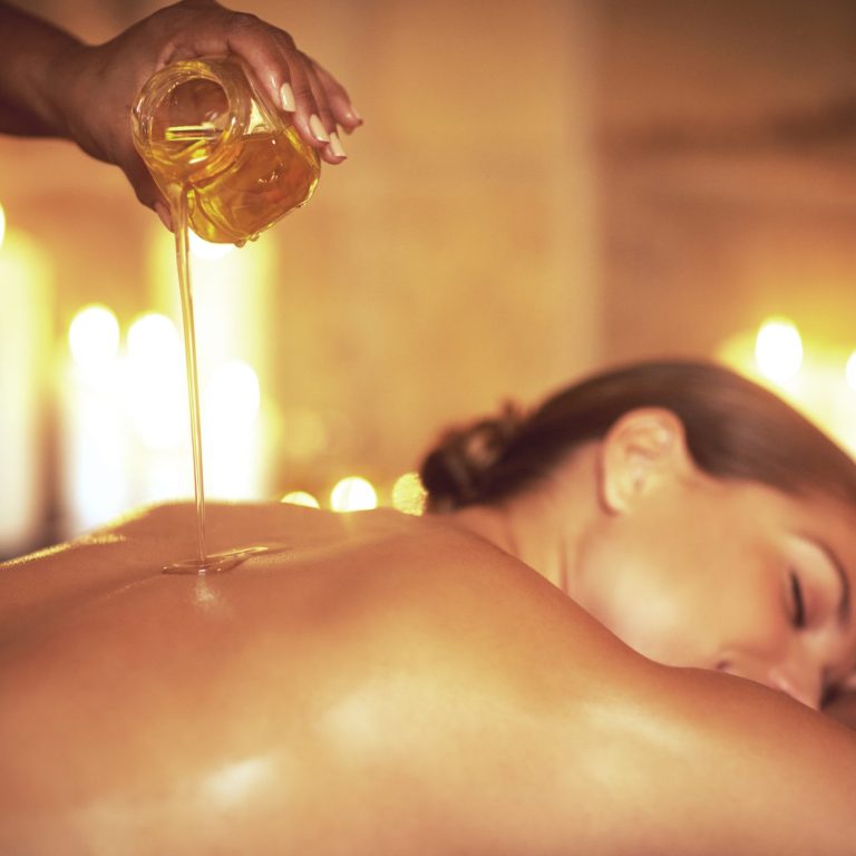 Shot of a masseuse pouring oil on a womans back before her massage.